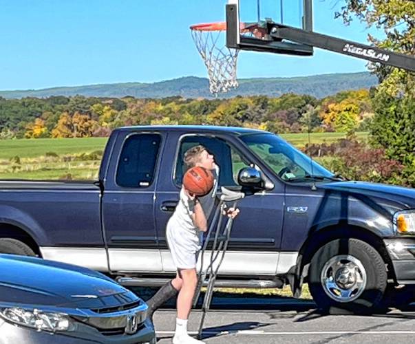 Owen Earle shoots hoops while on crutches outside of his house in Hadley.