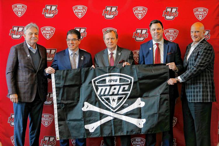 UMass football head coach Don Brown, from left, Chancellor Javier Reyes, MAC commissioner Jon Steinbrecher, Athletics Director Ryan Bamford and men’s basketball head coach Frank Martin hold the conference’s pirate flag, part of a new tradition begun in 2018. The flag is meant to be flown at home after MAC teams pull off huge wins like beating a Power 5 team or winning a bowl game.
